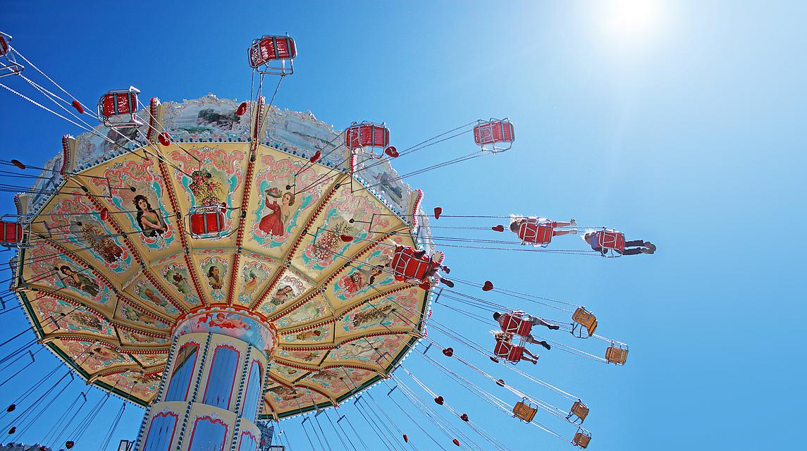 Ein Volksfest-Karussell dreht sich unter strahlend blauem Himmel.